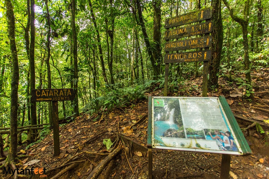 Rio Celeste waterfall sign. Photo of a billboard about Rio Celeste, a sign that says "Catarata 350 meters" pointing left and another wooden sign behind the billboard 