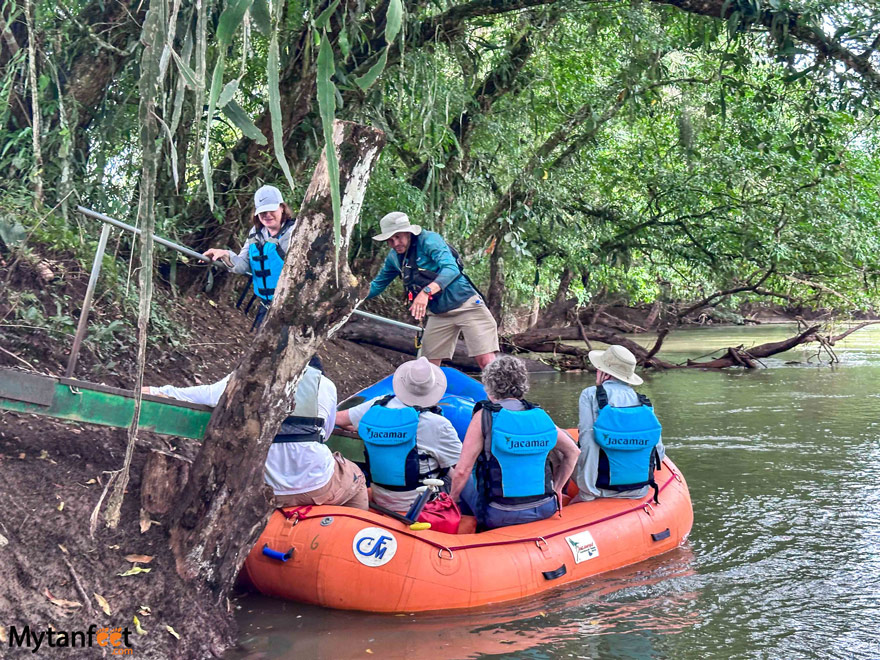 A group of elderly Caucasian tourists sitting on an inflatable raft, with a tour guide helping them get off and back onto the river bank - on the Pure nature safari float tour in Costa Rica 