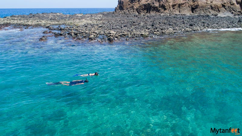 two people are snorkeling in clear turquoise waters, near a large rocky reef - best day trips from WEstin Conchal, a private flaming snorkeling tour