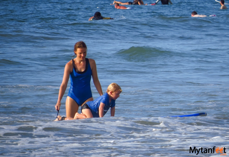 Things to do in Tamarindo - surf lessons. A mom is helping her young son on a surf board at the beach in Costa Rica
