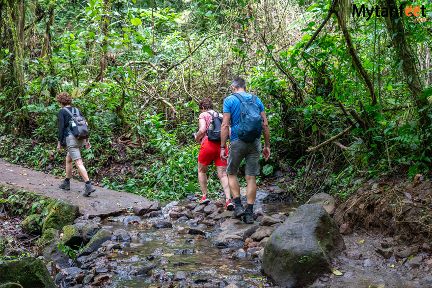 Rio Celeste trail. Two women and one man in hiking gear is crossing a small creek in a rainforest 