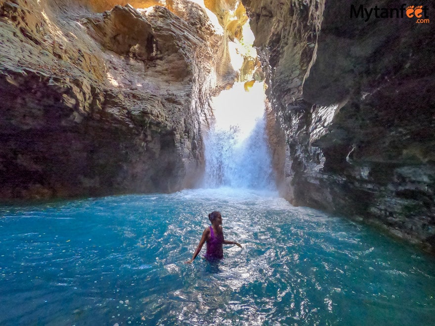 la leona waterfall hike. A woman wearing a purple shirt is standing in a blue waterfall pool in a cave in Costa Rica 
