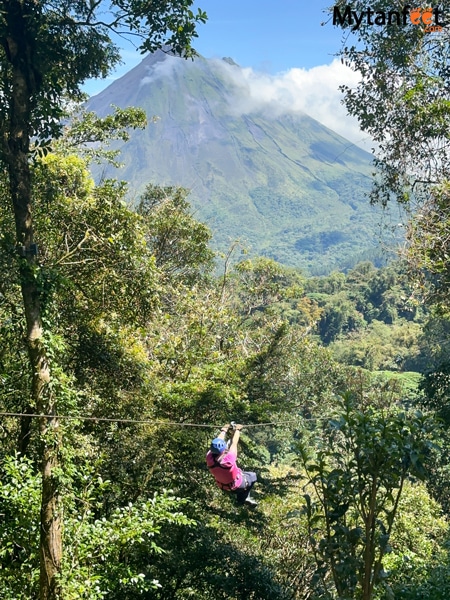 An adult is ziplining through the rainforest with Arenal Volcano as a backdrop (at sky Adventures in La Fortuna, Costa Rica).