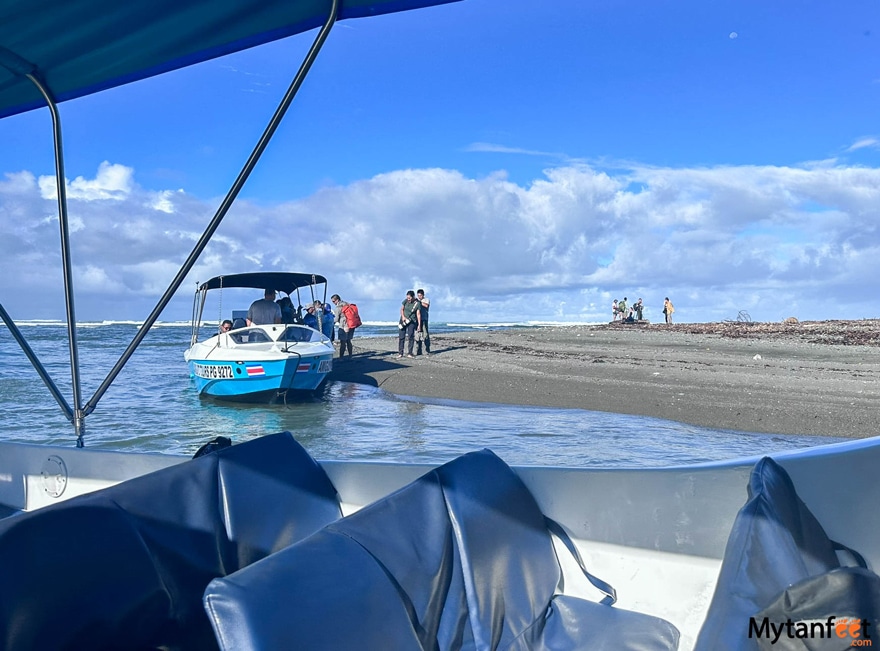 From the perspective of someone inside a boat, looking out at a speed boat on the shores of a beach, people are getting off the boat in Corcovado National Park, Costa Rica 