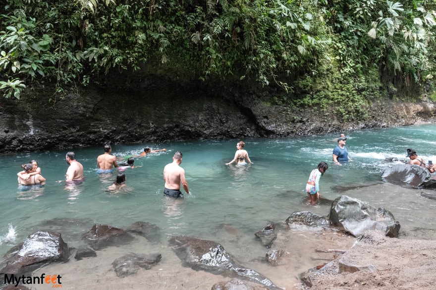 People are swimming in an emerald green river, of the La Fortuna waterfall in Arenal