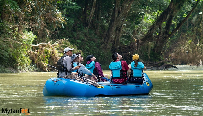 safari float at penas blancas river - a group of adults are sitting in a raft wearing lifejacket, floating down a green river looking up at the trees 